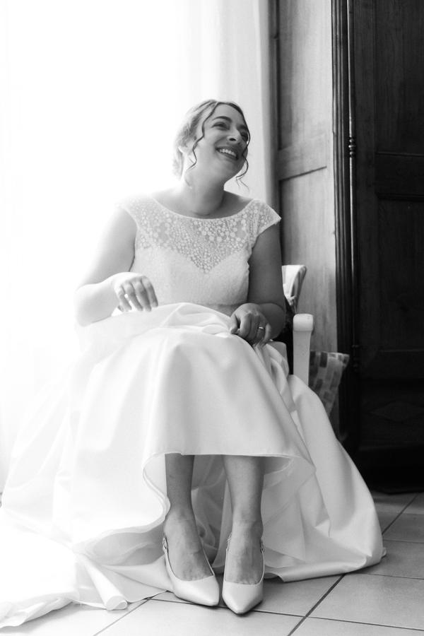 La mariée rit, assise près d'une porte, en noir et blanc