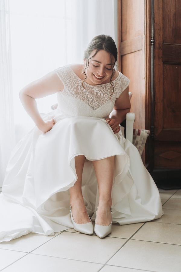 La mariée enfile ses chaussures, assise près d'une fenêtre