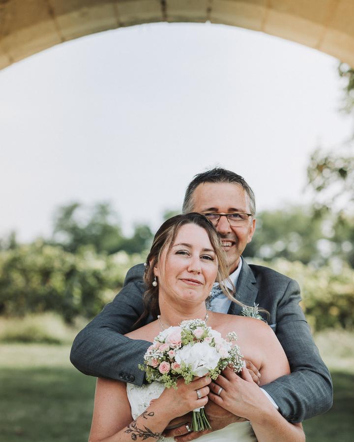 Le marié enlace la mariée par derrière sous une arche en pierre