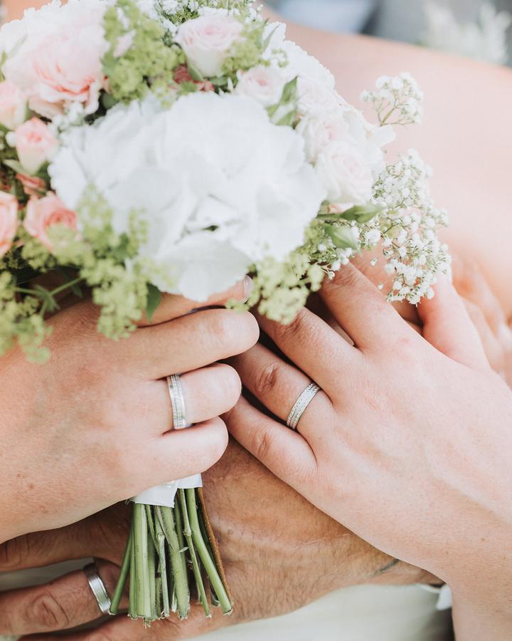 Les mains des mariés et leurs alliances sur le bouquet