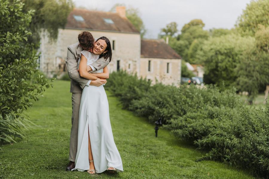 Le marié enlace la mariée qui rit, devant un vieux moulin en pierre