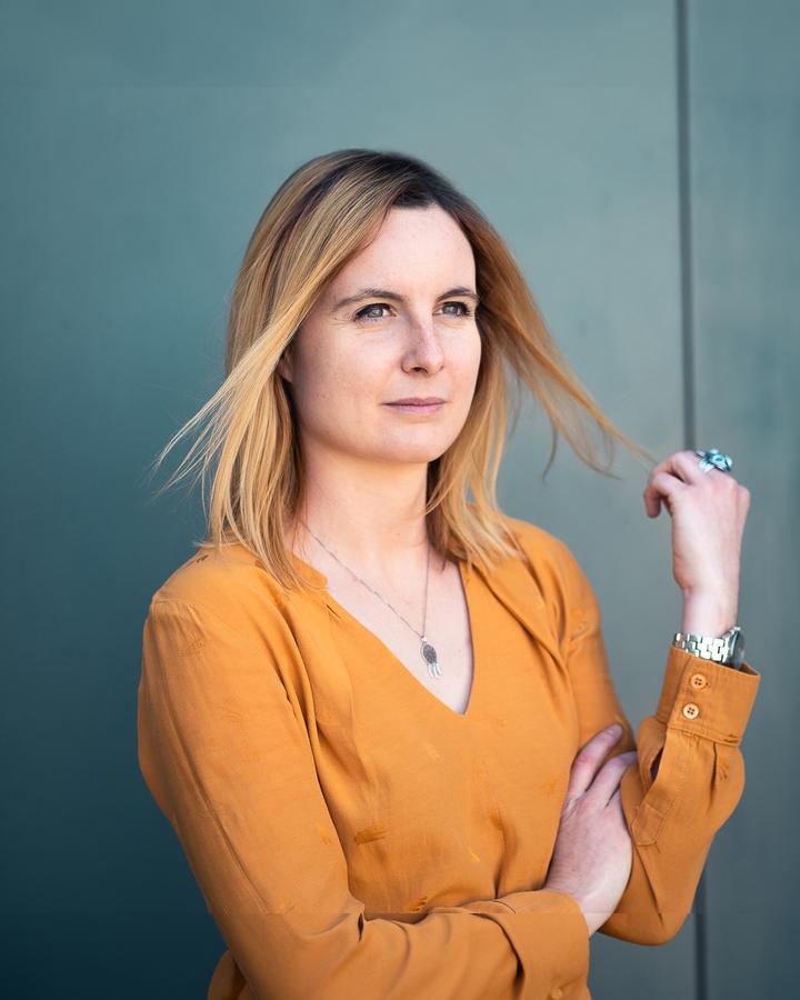 Femme en blouse orange devant un mur bleu-vert