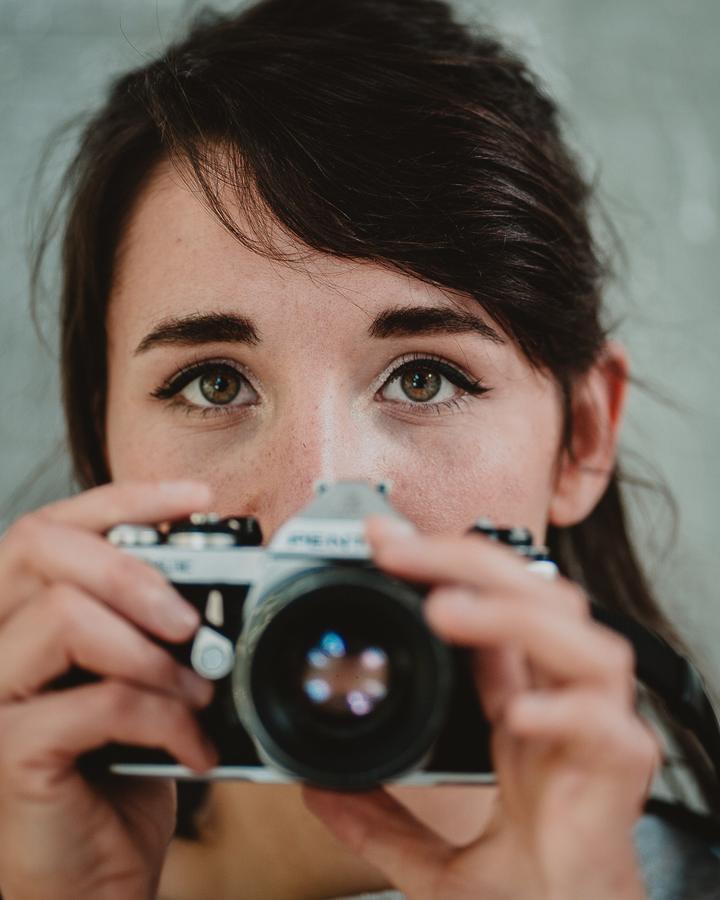 Une femme tient un appareil photo argentique devant son visage
